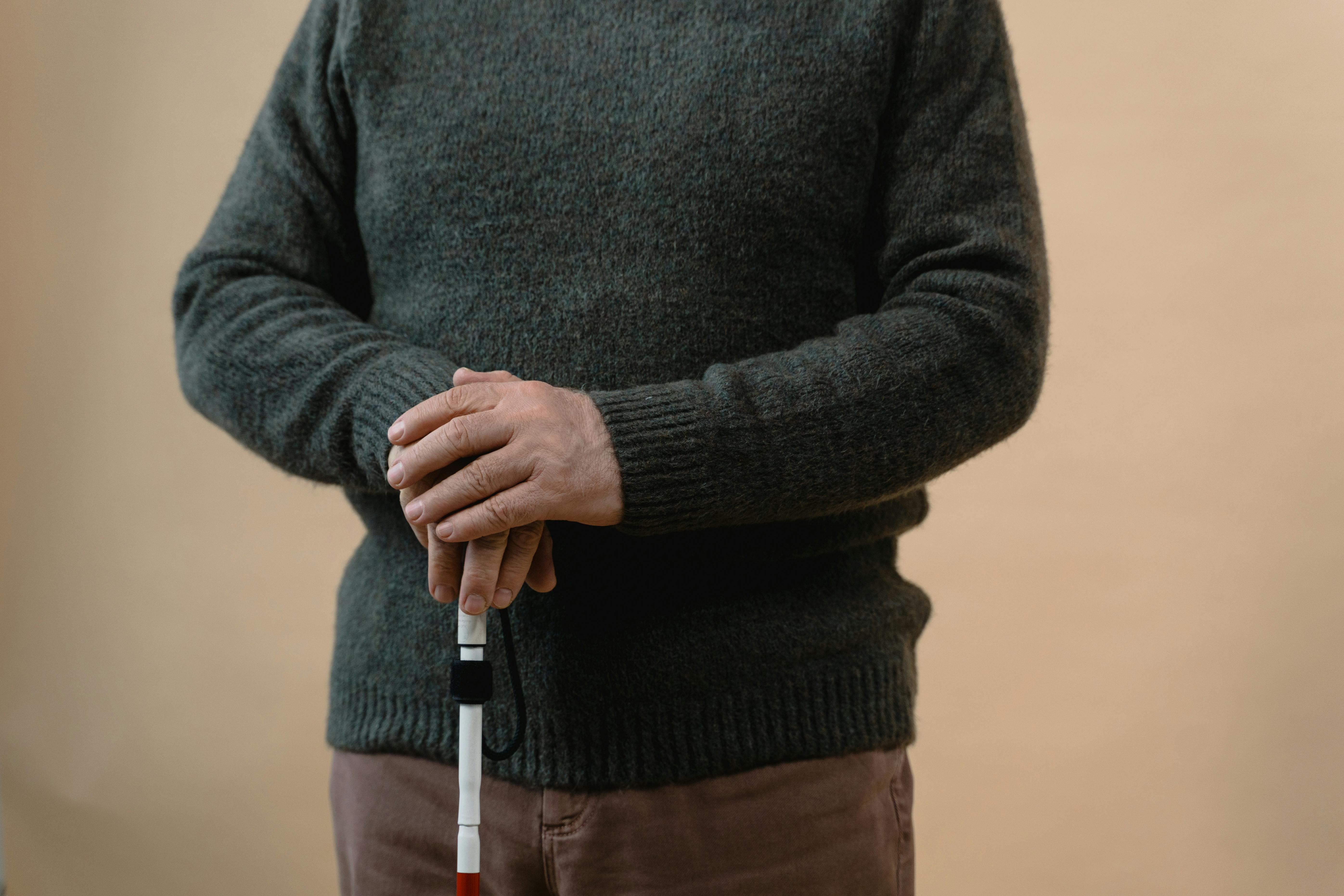 A man in a sweater holding a white cane, symbolizing vision impairment.