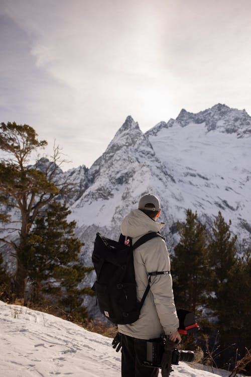 Free A Person with Backpack Holding a Camera on a Snow Covered Mountain Stock Photo