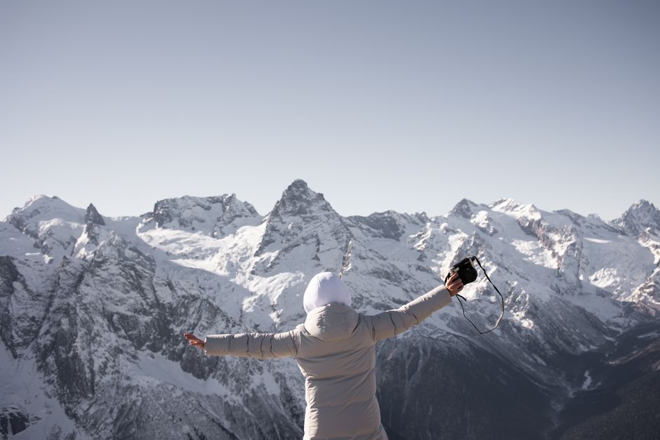 Person enjoying a snowy mountain view, capturing the moment with a camera.