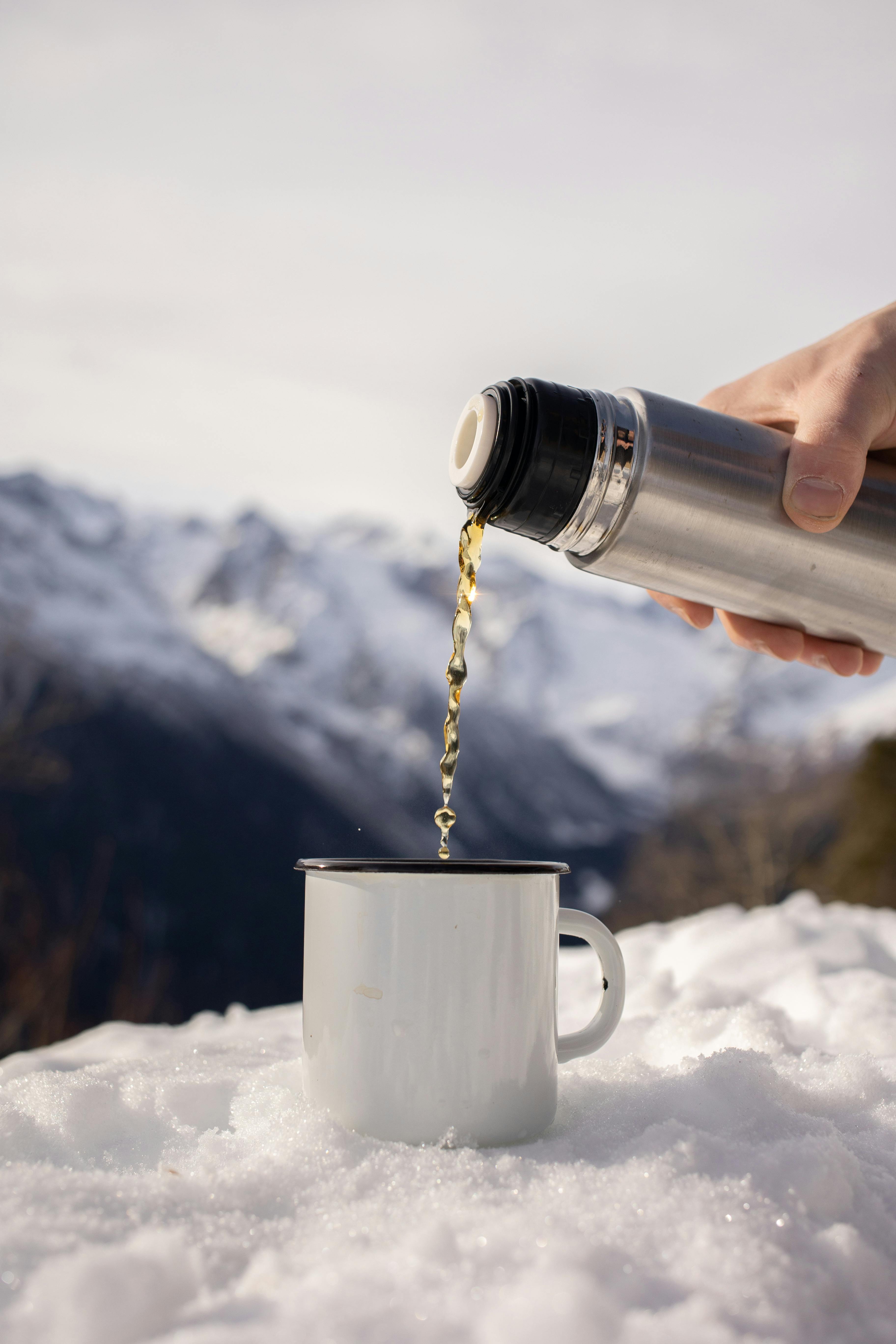 Pouring hot tea from a thermos into a cup in the mountains. Stock