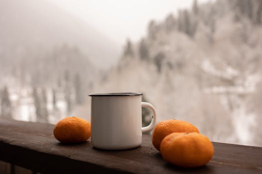 White mug with fresh oranges on a snowy balcony view, perfect winter warmth.