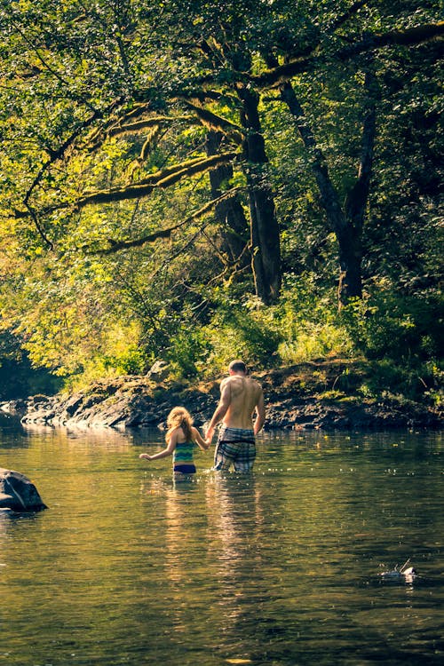 A Man and a Child Walking Hand in Hand in a River