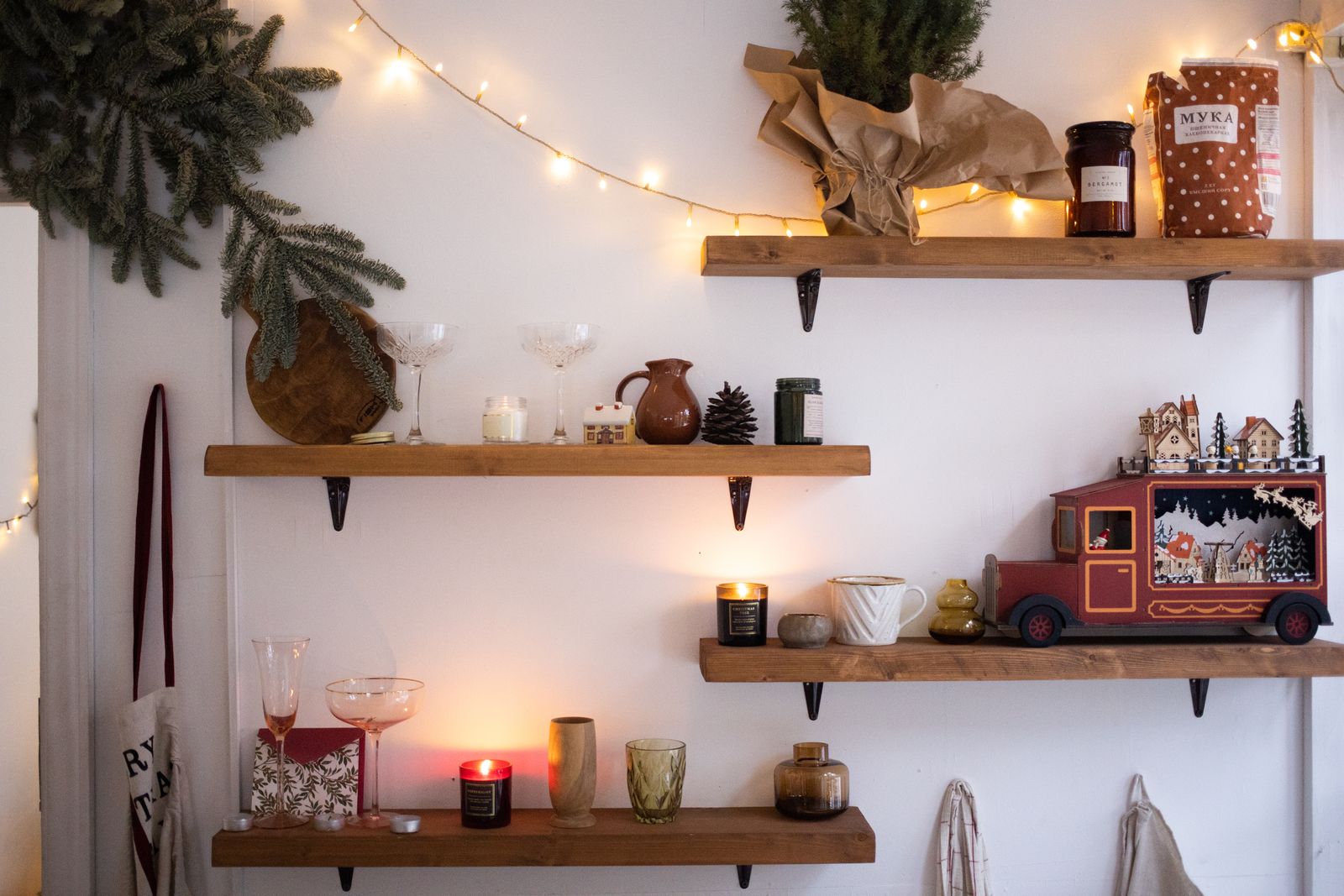 wooden floating shelves with candles, miniature houses, pine branches and string lights
