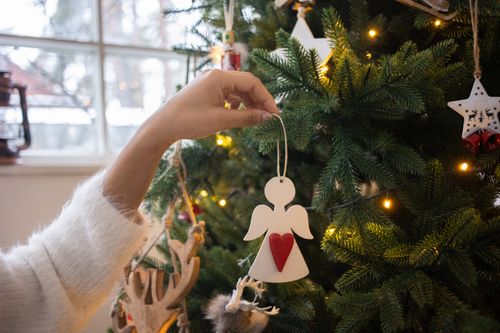 Free Close-up of a hand placing an angel ornament on a Christmas tree indoors. Stock Photo