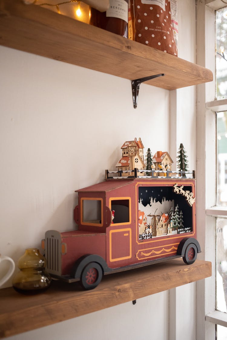 A Christmas Ornament Of A Car With Houses And Trees On A Wooden Shelf