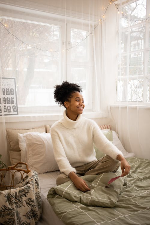 Free A Woman in White Sweater Sitting on the Bed Stock Photo