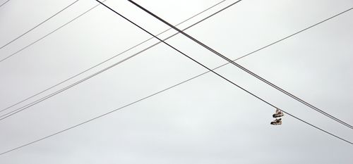 Free A pair of sneakers hanging on intersecting power lines against a cloudy sky, creating a minimalist urban scene. Stock Photo