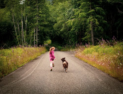 A Girl in Pink Sports Wear Running on a Road with a Dog