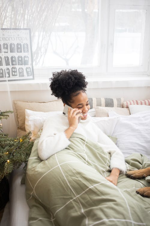 Free A Woman Lying in Bed Beside a Christmas Tree Talking on the Phone Stock Photo