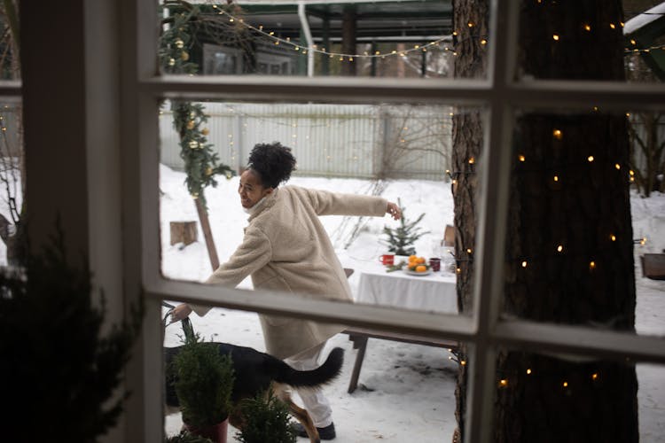 A View From A Window Of A Woman Holding A Black Dog On Snow Covered Ground