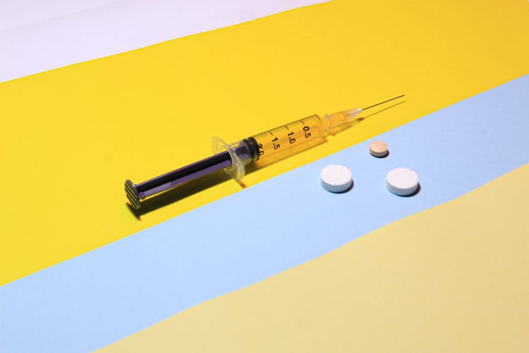 A Syringe With Liquid Beside Round Pills