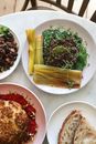 Top view of delicious vegetarian dish with pickled stems near buckwheat porridge with green herbs on plate on table near bread and whole roasted cauliflower in light room near chair