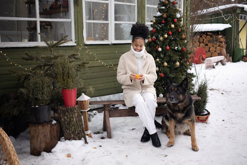 A Woman in Winter Clothes Sitting on a Wooden Bench Beside a Dog