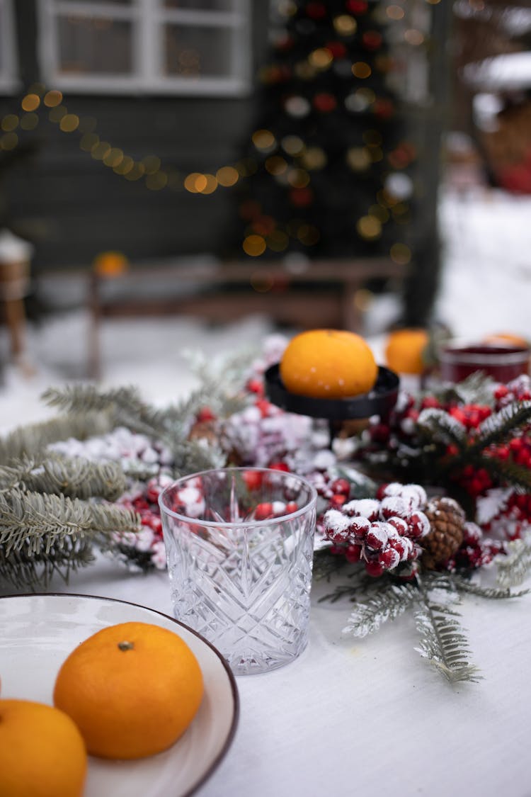 Mandarin Fruits And A Drinking Glass On A Table With Christmas Ornaments