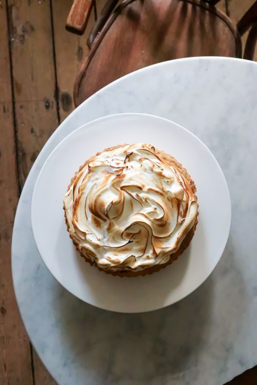 Free Top view of delicious pie with meringue on plate placed on round white table near chair on wooden floor in light place Stock Photo