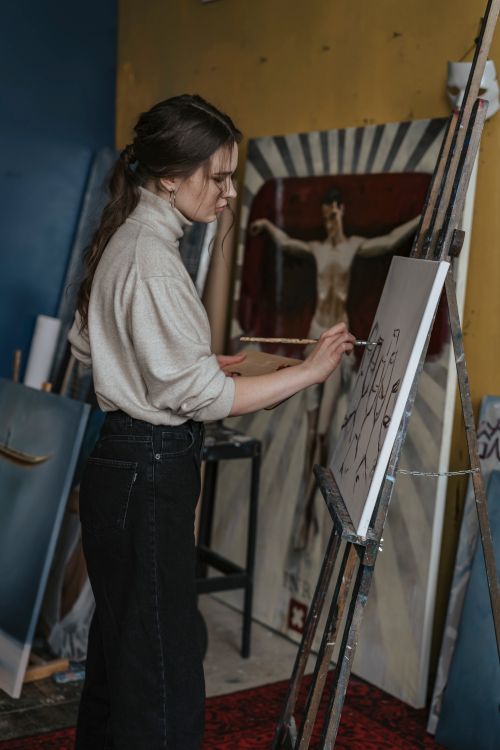 Free A woman artist deeply engrossed in painting on a canvas set up on an easel in her studio. Stock Photo