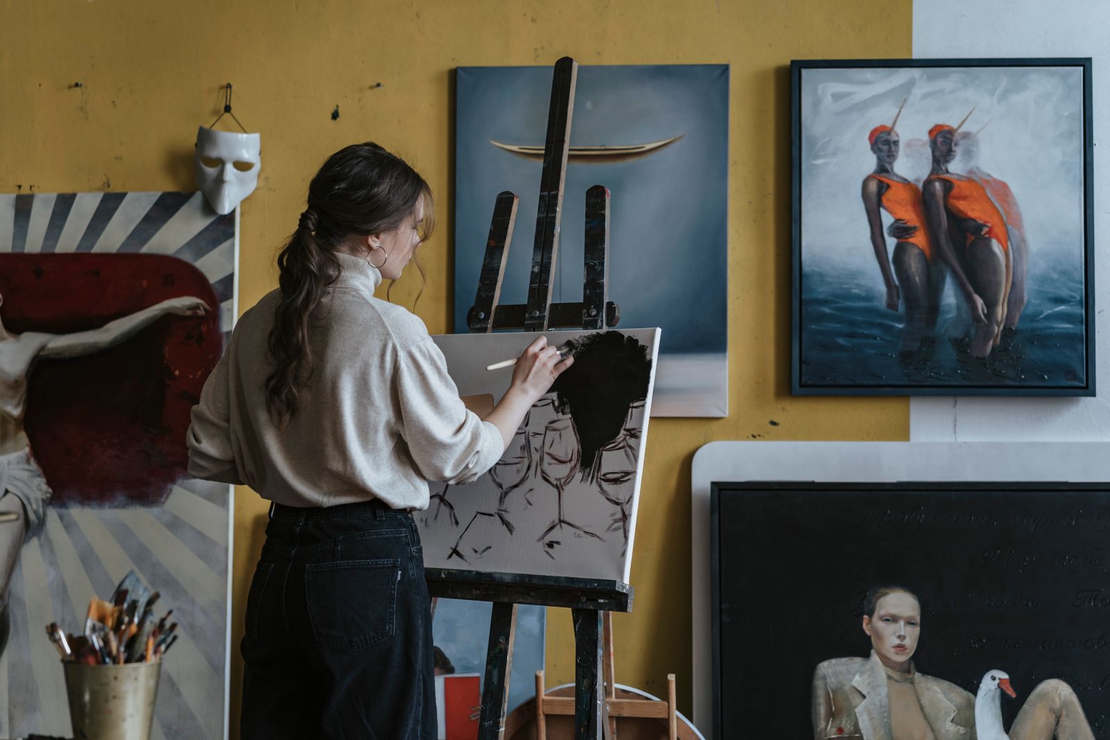 Painter working at an easel in a studio hung with canvases — photo by olia danilevich on Pexels