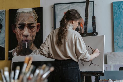 Free Female artist working on a canvas in a studio with paintings in the background. Stock Photo