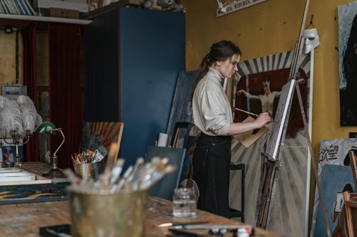 Free Caucasian woman painting in an art studio, surrounded by artistic tools and canvases. Stock Photo