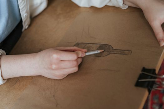 A person sketching a wine bottle on paper with a pencil. Artistic process in a creative setting.