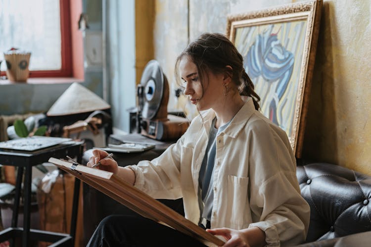 Teenage Girl Sitting On A Couch Making A Drawing On Wood Canvas Board