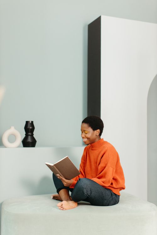 Free A young woman with afro hair enjoys reading a book on a modern couch indoors. Stock Photo