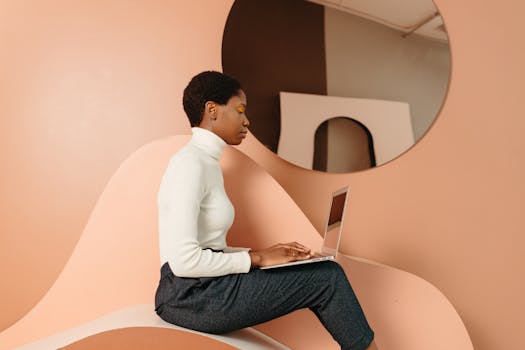 Side view of African woman in modern setting working on laptop, showcasing remote work lifestyle.