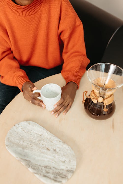 A Person in Orange Sweatshirt Holding a Mug beside a Coffee Brewer