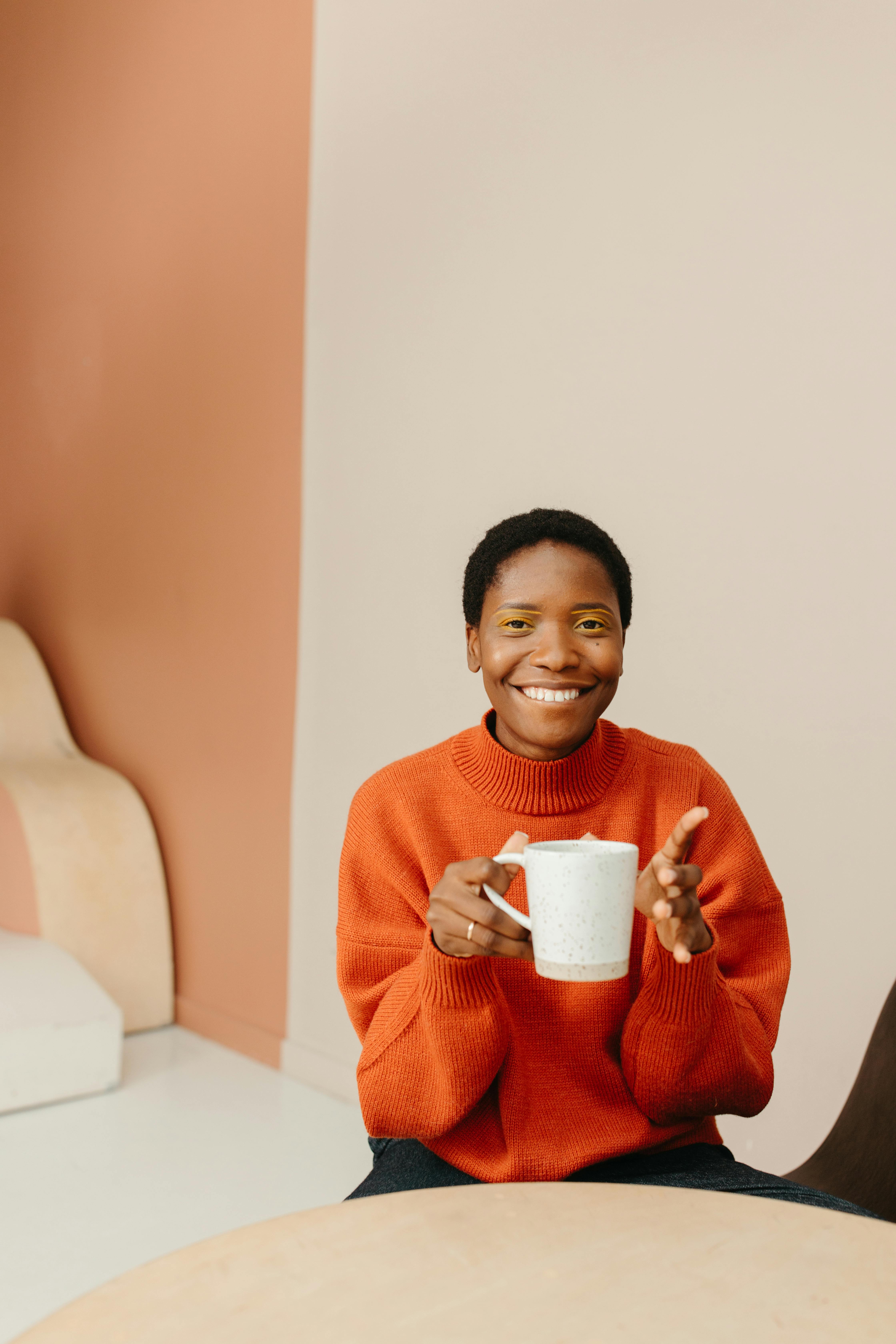woman in orange sweater holding white ceramic mug smiling