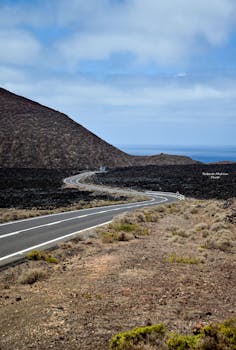 Curving road through Lanzarote's volcanic terrain under a blue sky, showcasing natural beauty.