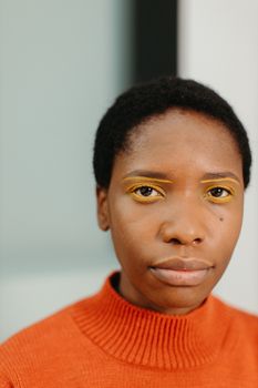 Close-up portrait of a woman wearing vibrant yellow eye makeup and orange sweater, emphasizing strong colors.