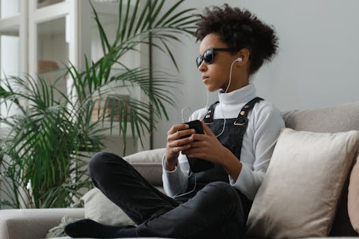 Young girl with sunglasses listening to music indoors on a sofa.