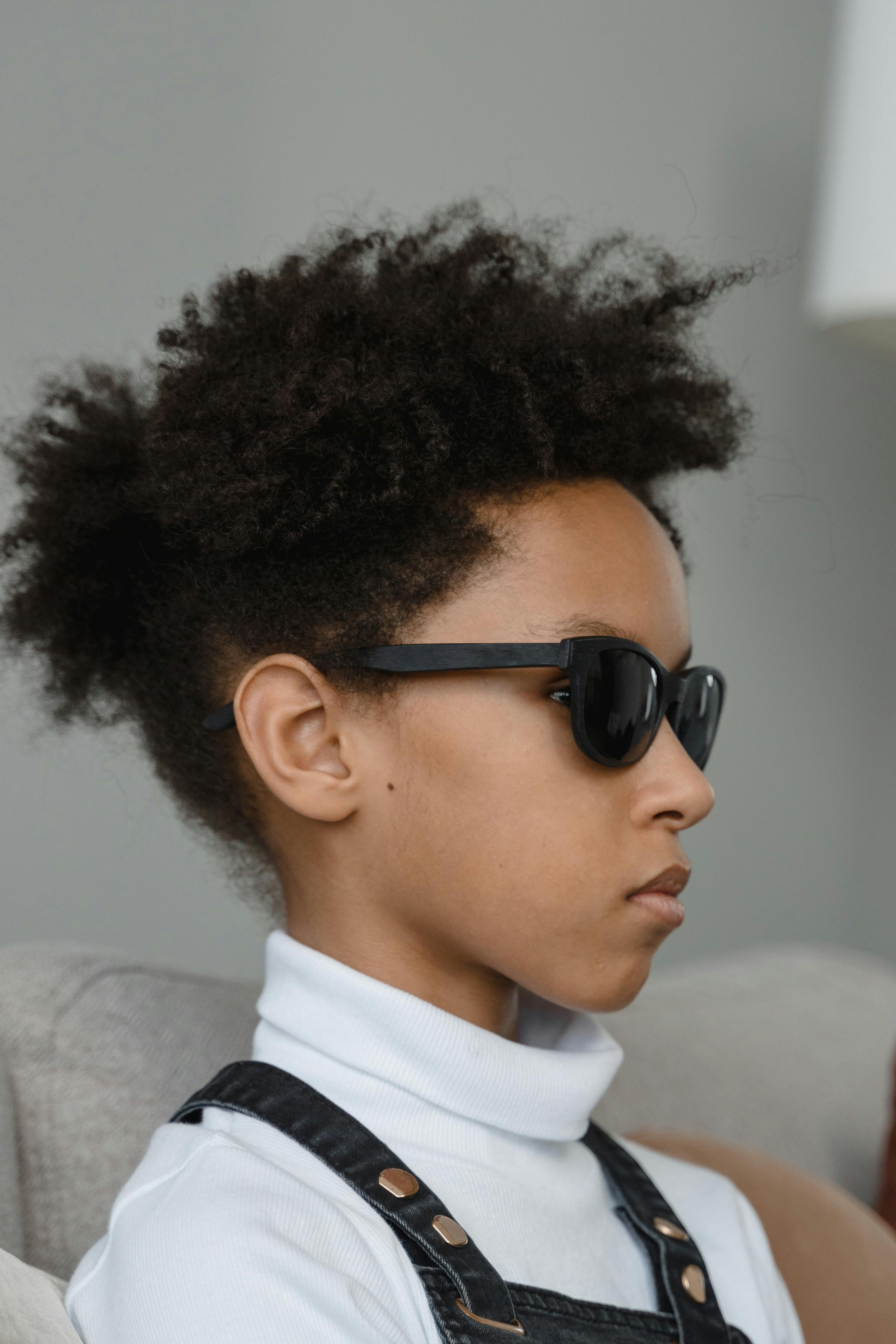 Side profile portrait of a young girl wearing sunglasses, showcasing her distinctive afro hair and style.
