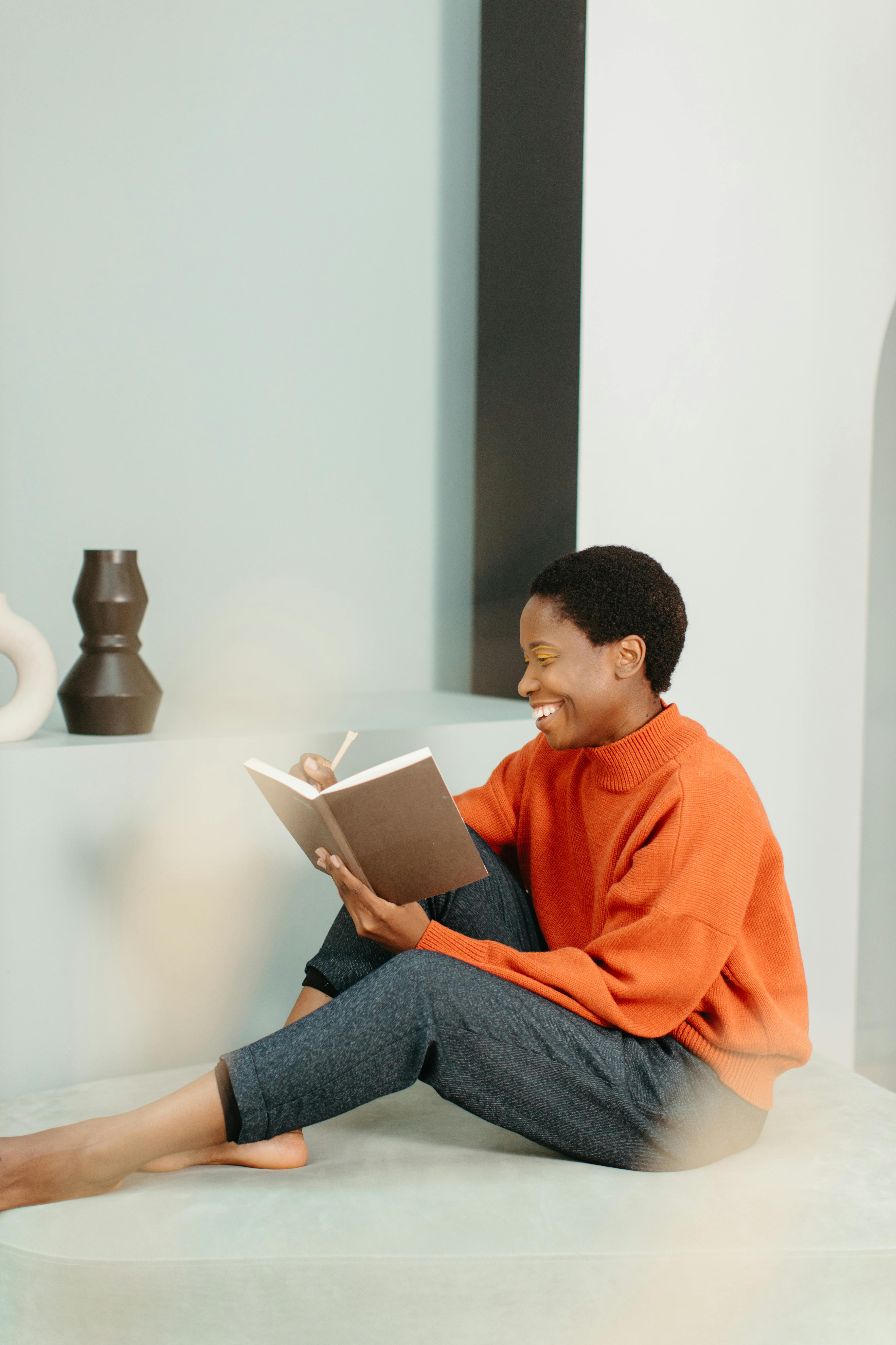 a woman in orange sweatshirt writing on a notebook