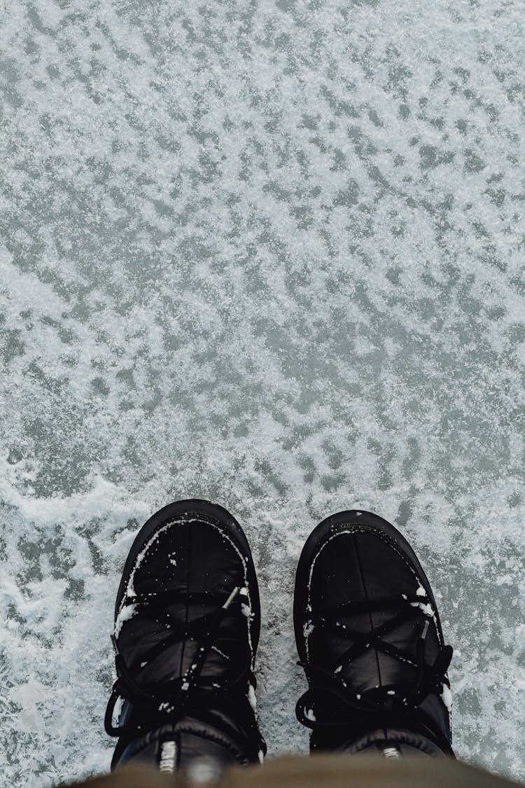 A Person Wearing Black Boots On A Snow Covered Road