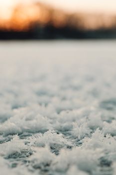 A close-up view of frost-covered snow during sunrise, showcasing delicate textures and a warm glow.