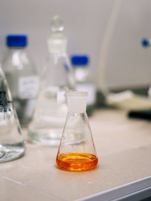 Free An Erlenmeyer flask containing orange liquid on a lab bench, surrounded by glassware. Stock Photo