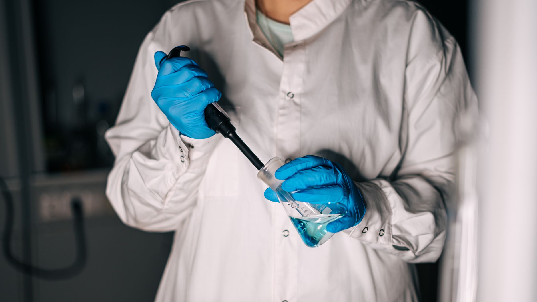 Scientist in a lab coat using equipment for a chemical experiment.