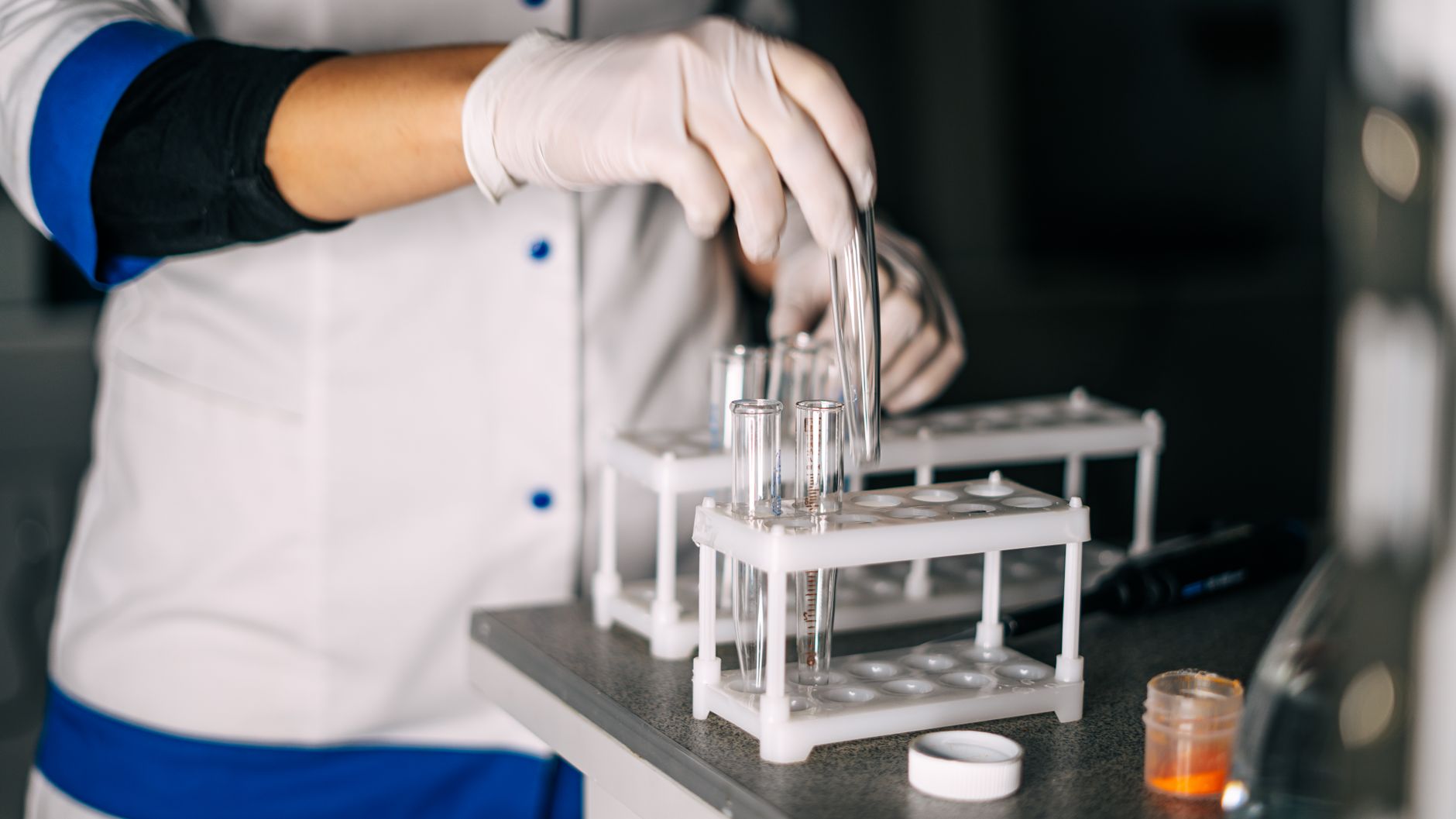 A scientist in a lab coat handling test tubes in a laboratory setting with a focus on equipment.