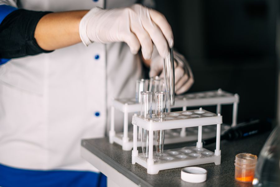 A scientist in a lab coat handling test tubes in a laboratory setting with a focus on equipment.