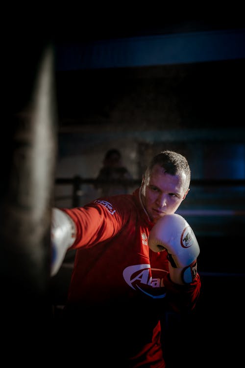 Free Powerful male fighter in gloves hitting heavy punching bag while training in boxing ring Stock Photo