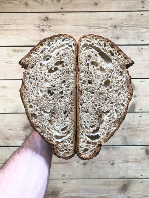 Free Overhead view of crop anonymous male with fresh homemade bread in hand near wooden surface in light place Stock Photo