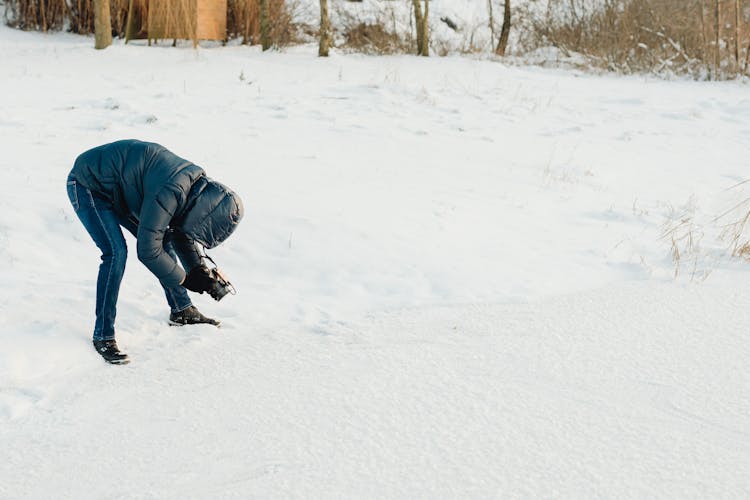 Woman In A Black Winter Jacket With A Hood Taking A Macro Shot With A Camera On Snow