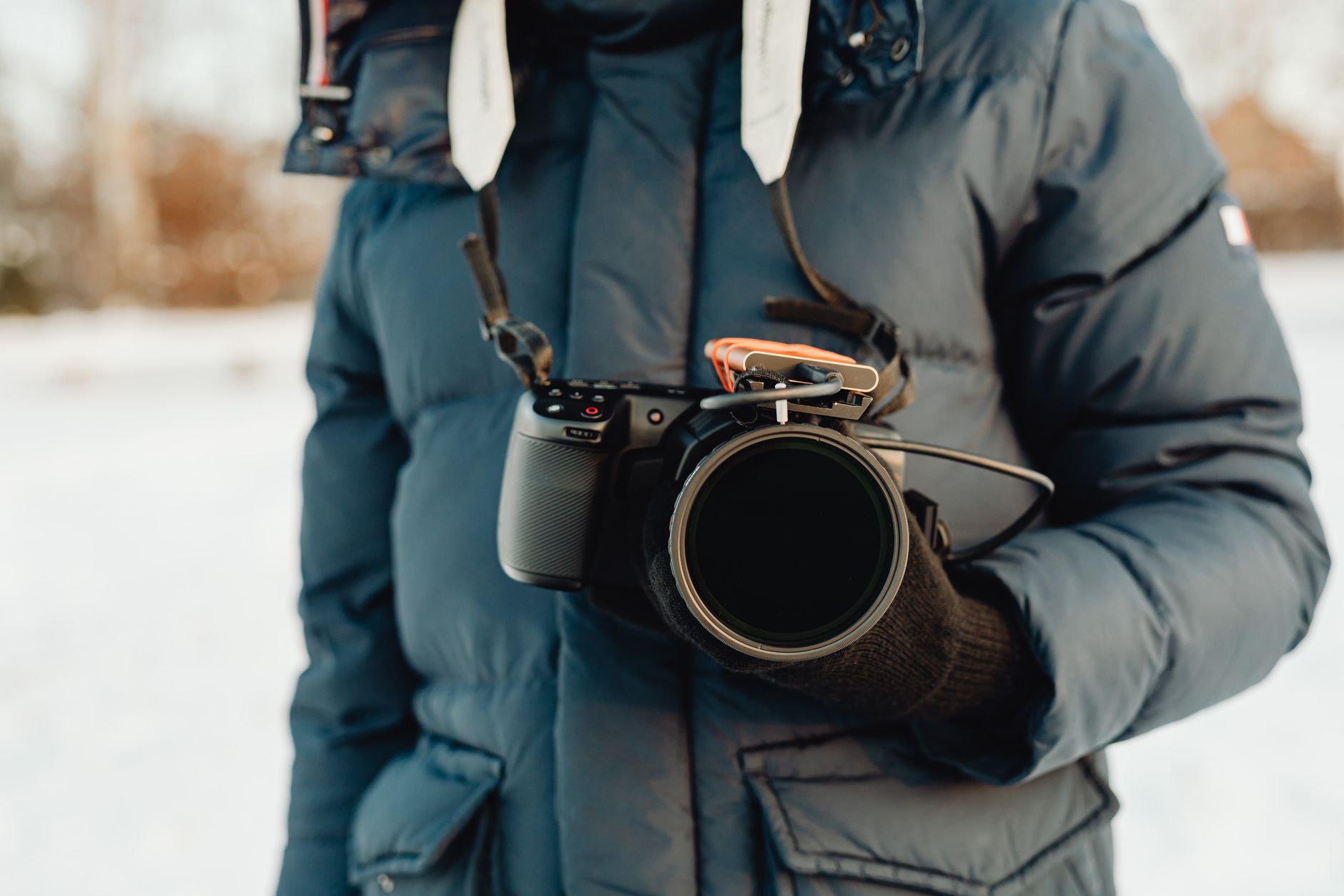 Photographer holding a camera in a winter setting, wearing a warm jacket.