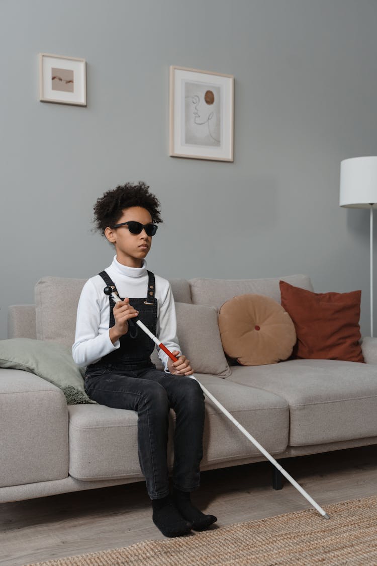 A Child With Visual Impairment Sitting On A Couch With A Stick