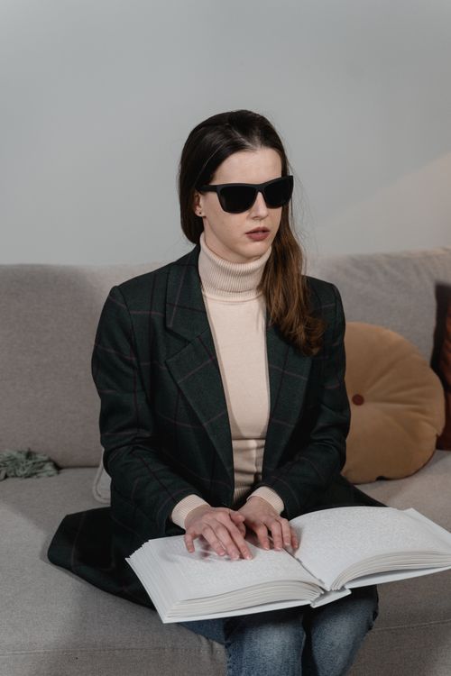 Free A woman with sunglasses reads a Braille book, focusing on tactile engagement. Stock Photo