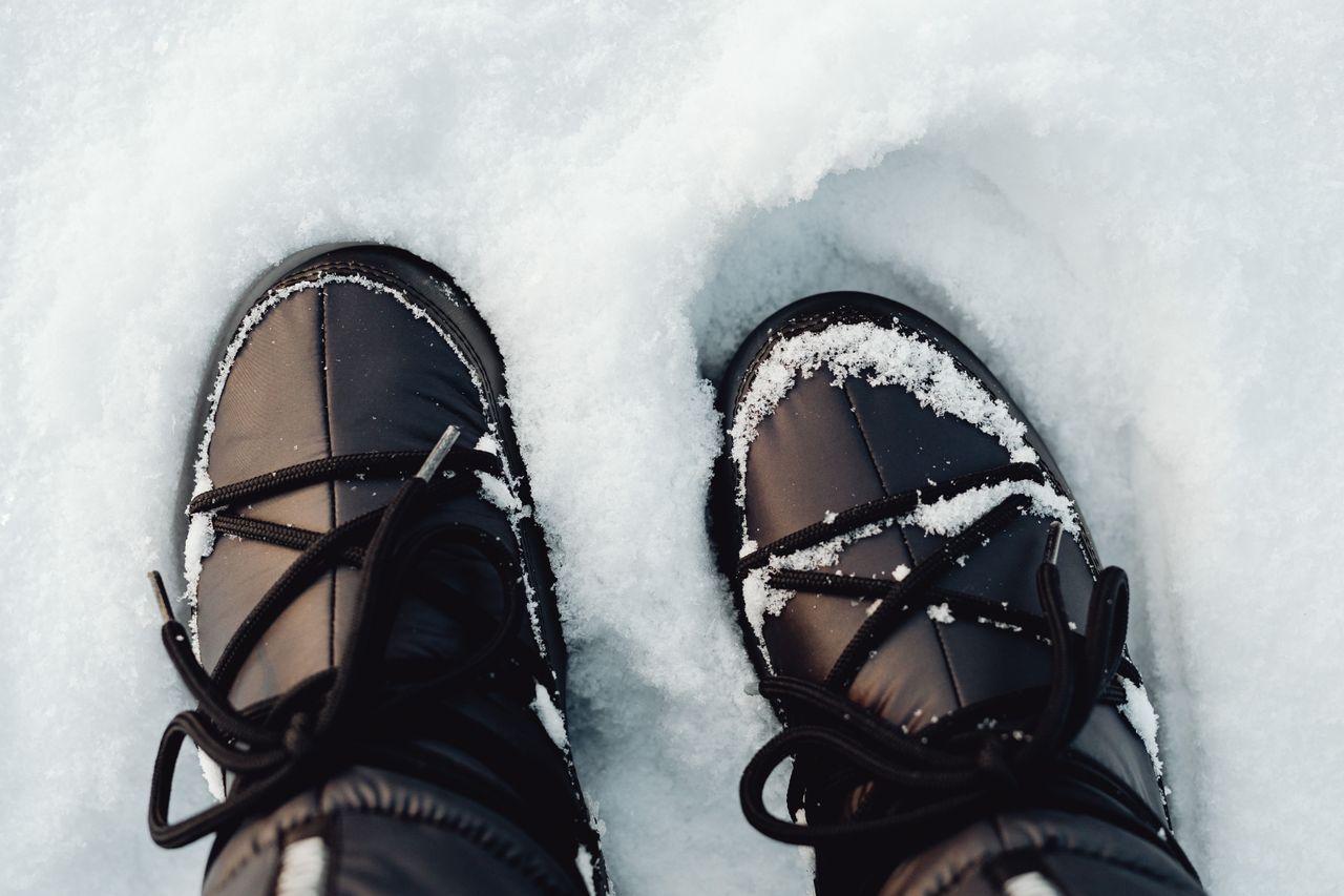 Black winter boots covered in snow seen from above