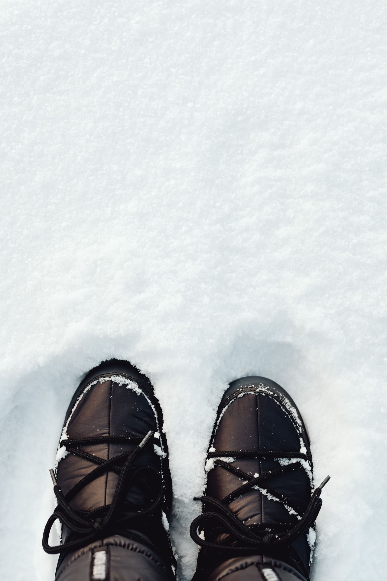 Black winter boots standing in fresh snow, top view