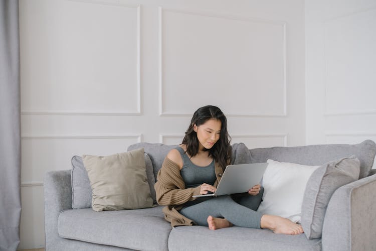 A Woman Sitting On A Couch While Busy Working On Her Laptop