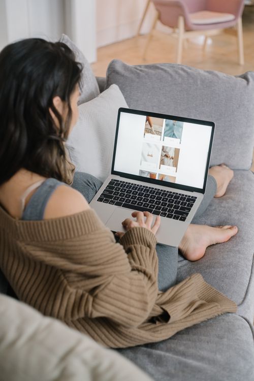 Free Woman sitting on a couch browsing on a laptop, embodying a cozy work-from-home lifestyle. Stock Photo
